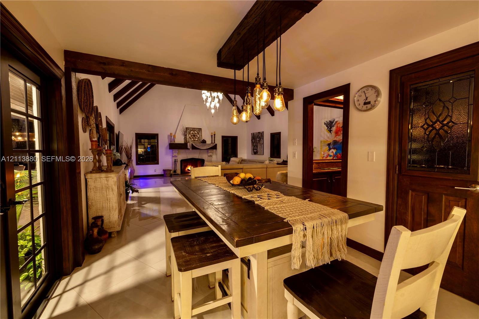 Dining area featuring exposed wooden ceiling beams, a custom multi-bulb pendant fixture, tile flooring, and a door with decorative glass inlay