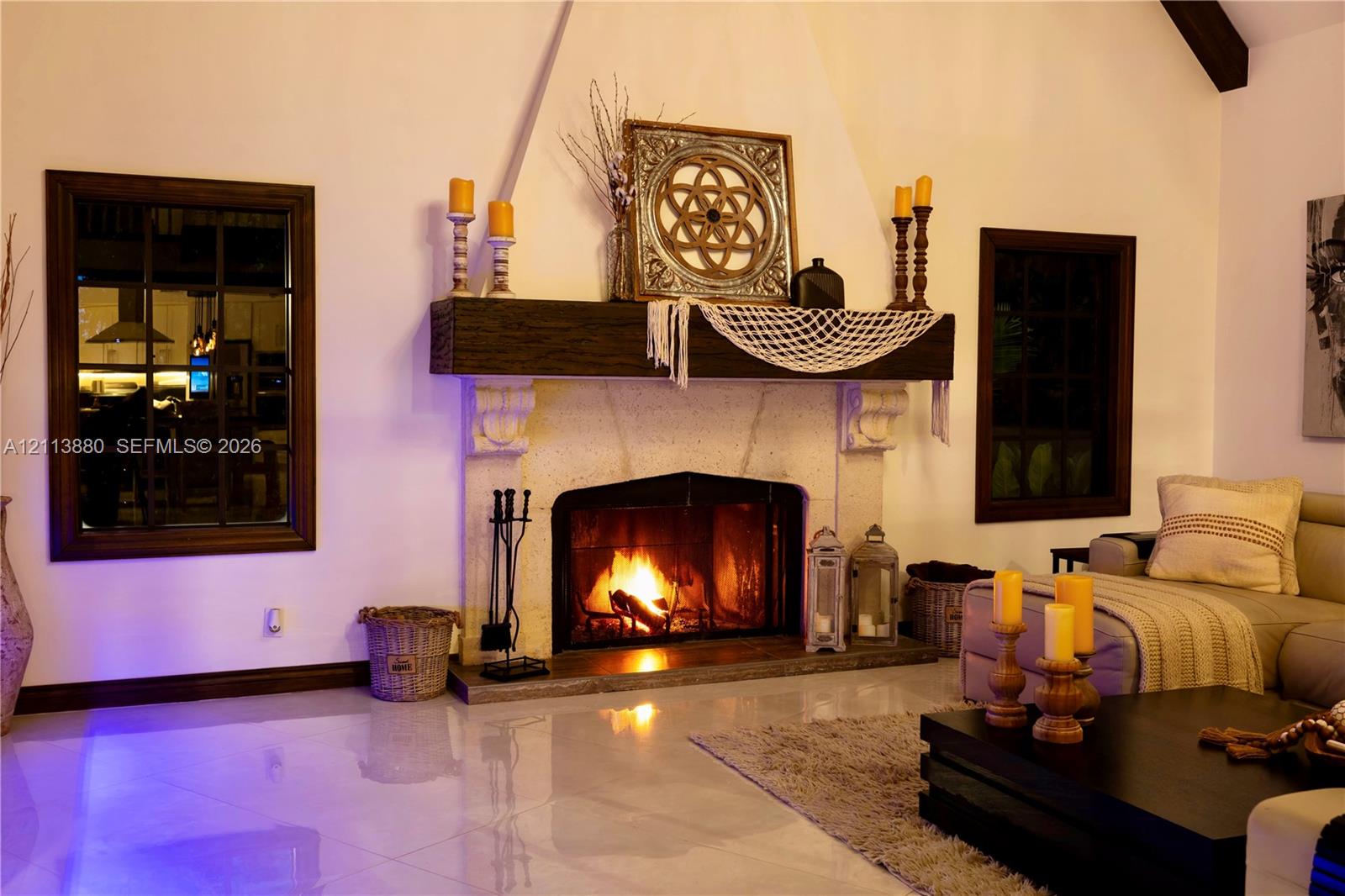 Floor-to-ceiling fireplace featuring a textured stone surround, heavy timber mantel, and vaulted ceilings, punctuated by dark-frame grid windows