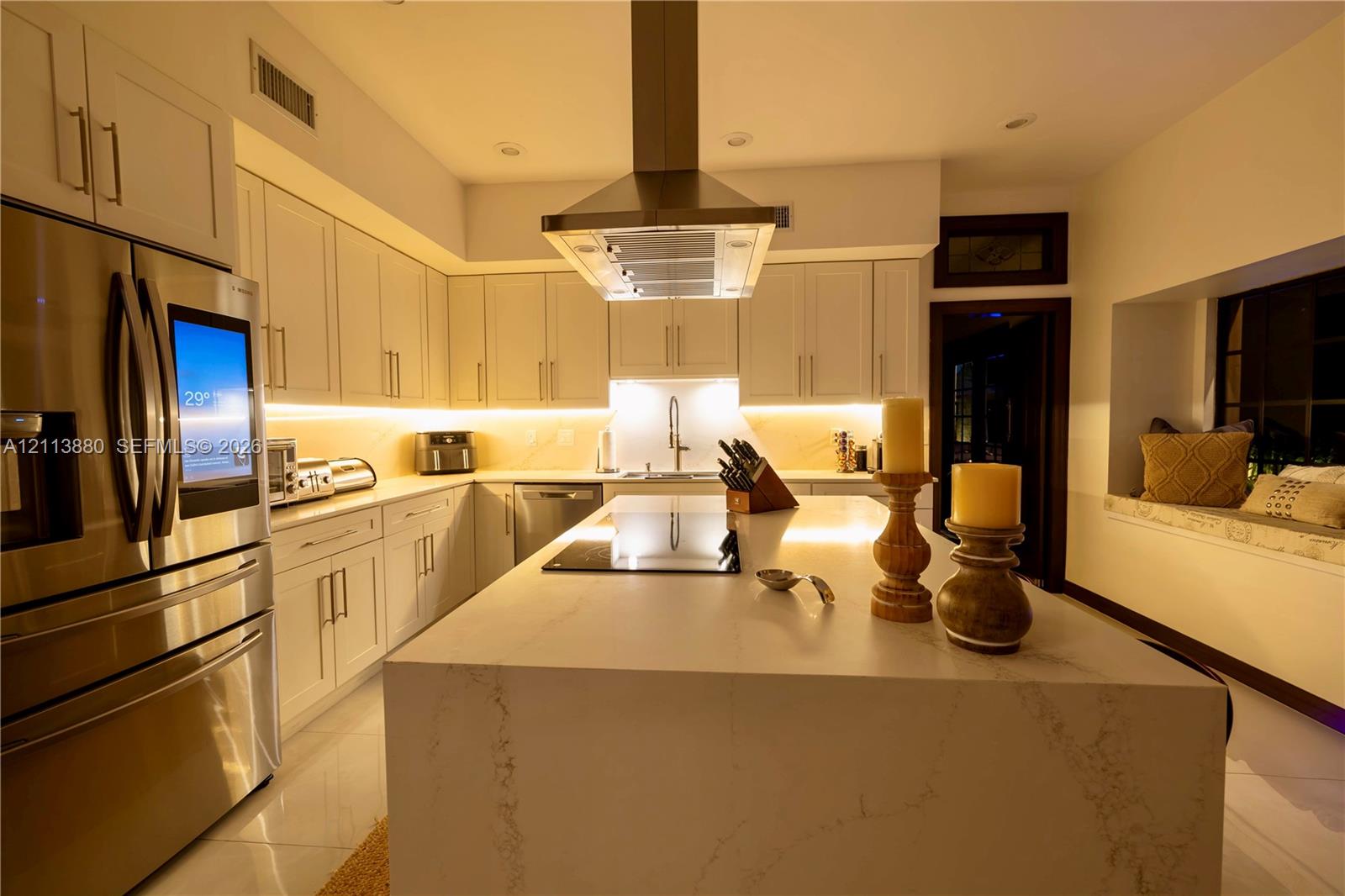 Kitchen featuring white cabinetry, an expansive center island with stone-finish countertops, stainless steel appliances, a ceiling-mounted range hood, and integrated under-cabinet lighting