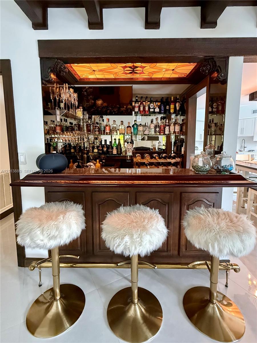 Built-in wet bar featuring mahogany-toned cabinetry, a polished wood countertop, mirrored backsplash, integrated display shelving, and an illuminated stained-glass ceiling inset