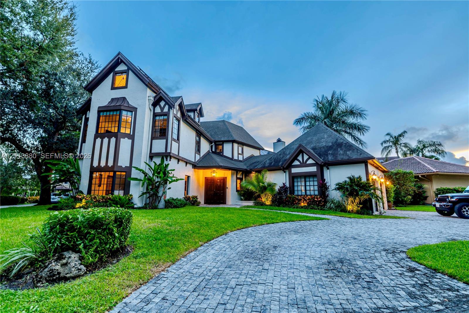 Tudor-inspired architectural exterior featuring stucco siding with timber accents, a multi-gabled roofline, a decorative bay window, and a paved cobblestone driveway