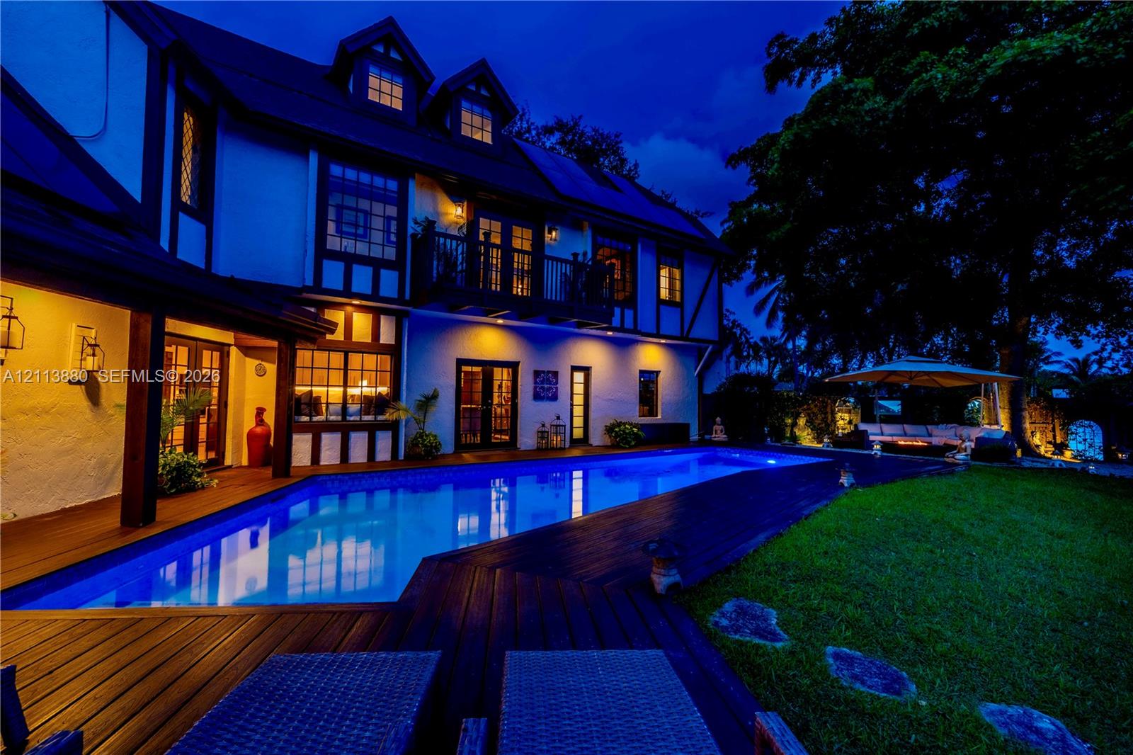 Tudor-style exterior featuring a rectangular inground swimming pool, expansive wood-finish decking, second-story balcony, and steep-pitched roofline with dormer windows