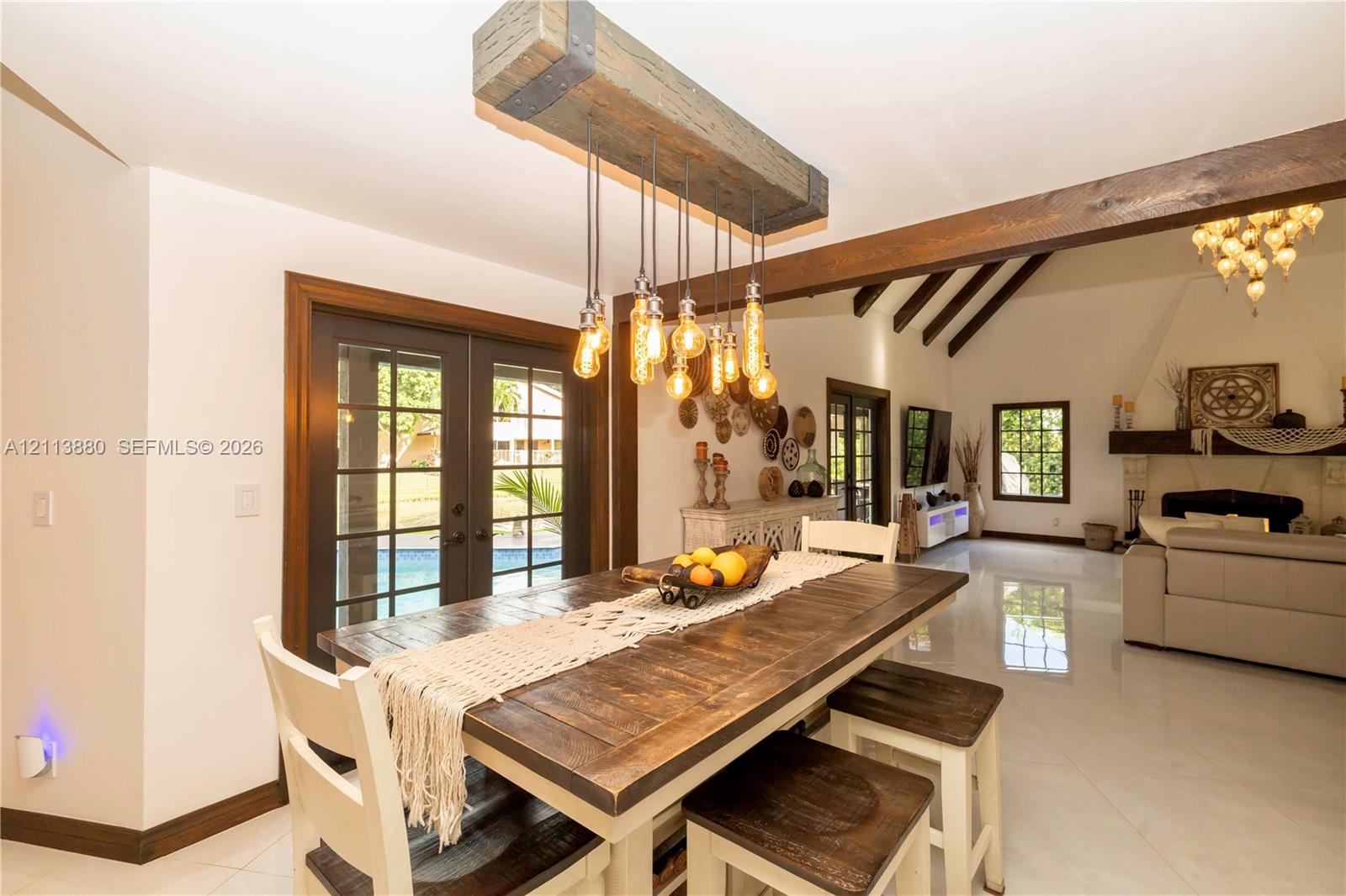 Custom timber beam lighting fixture with exposed filaments, dark-stained wood ceiling beams, multi-pane glass doors, and polished stone flooring