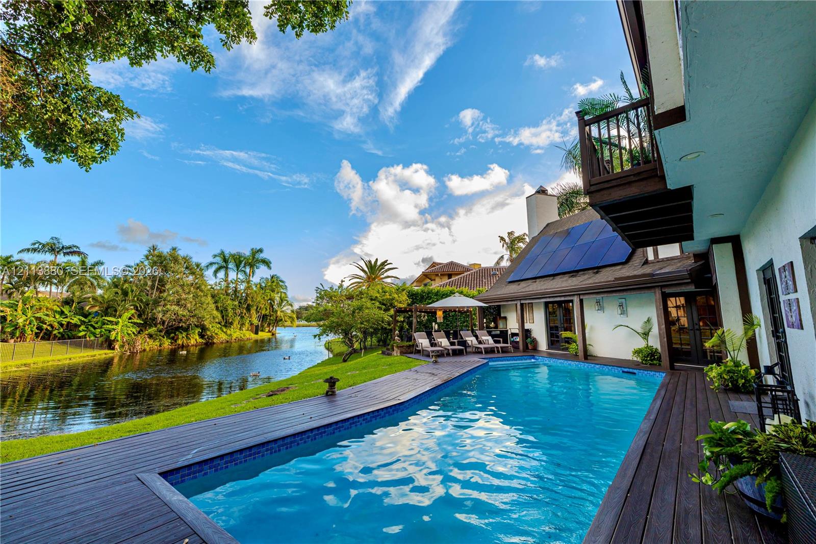 Waterfront backyard featuring a swimming pool, wood-finish decking, solar panels, and a second-story balcony