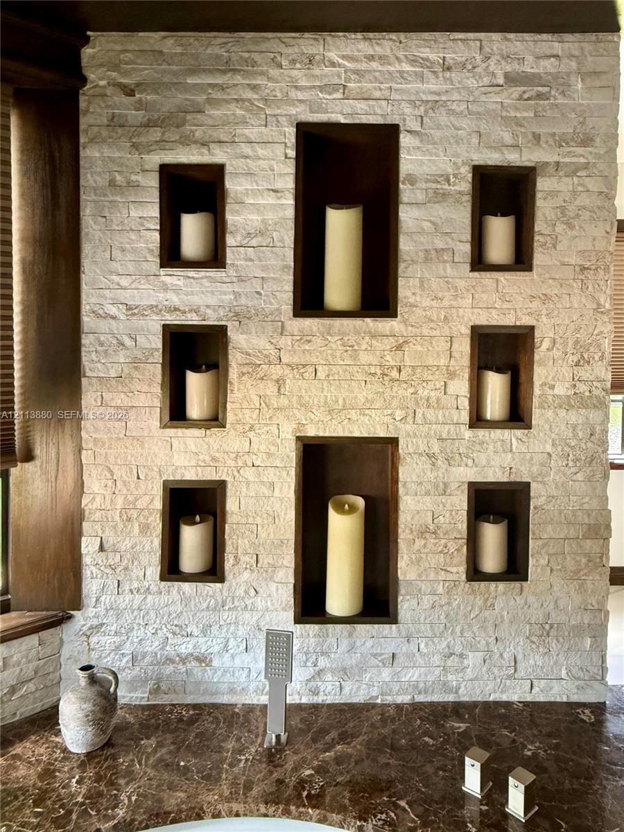 Stacked stone accent wall featuring six recessed niches with dark wood-finish trim, polished dark stone countertop, and brushed metal wall-mounted faucet