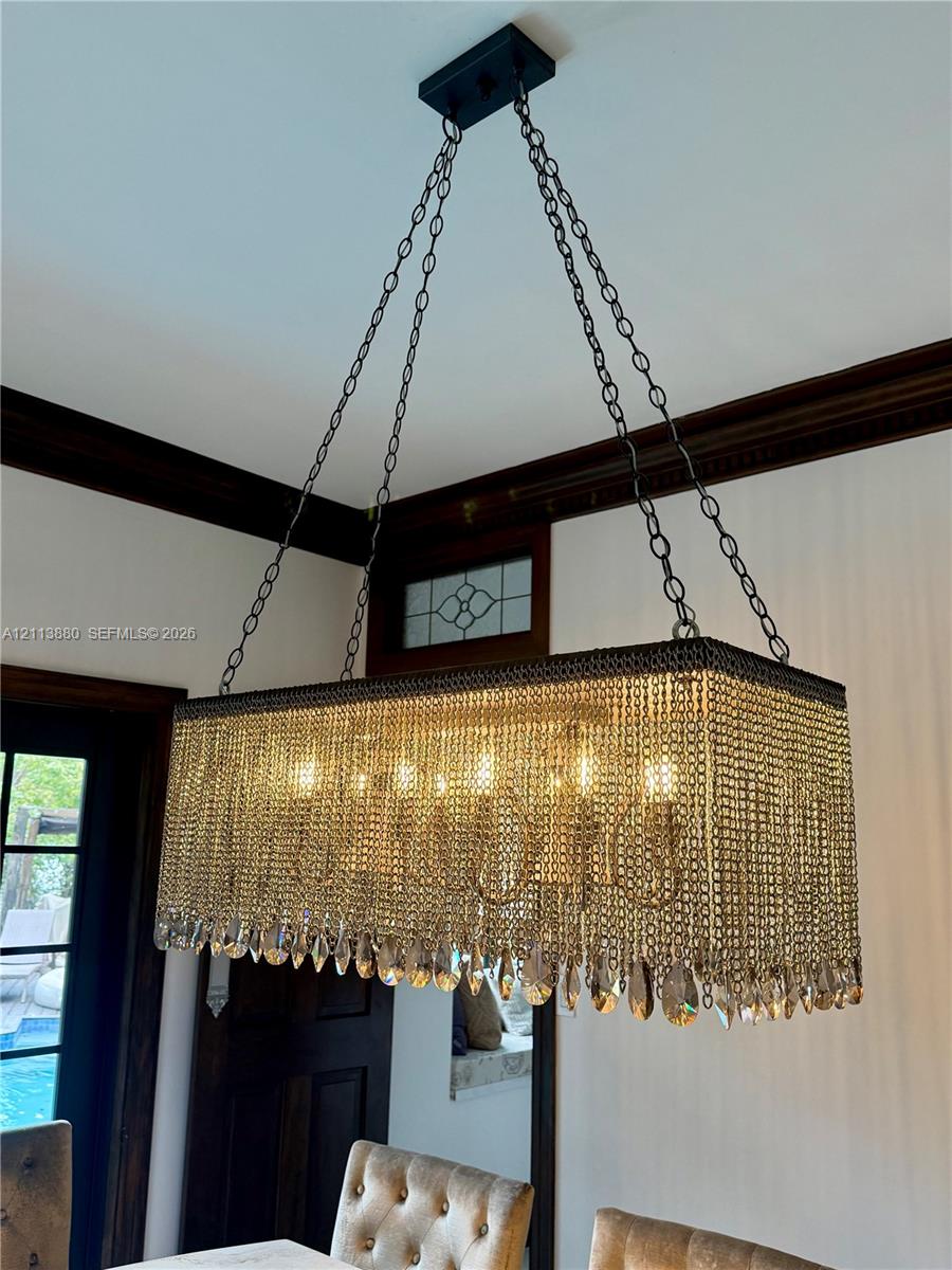 Rectangular chandelier featuring tiered crystal fringe, metal chain suspension, dark wood crown molding, and a transom window with leaded glass detail