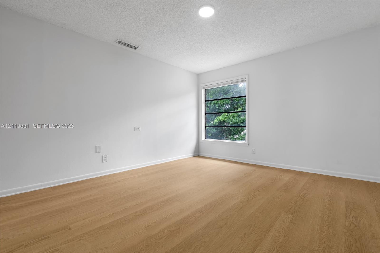 Room featuring wood-finish flooring, a single-pane window with dark frames, and a neutral color palette