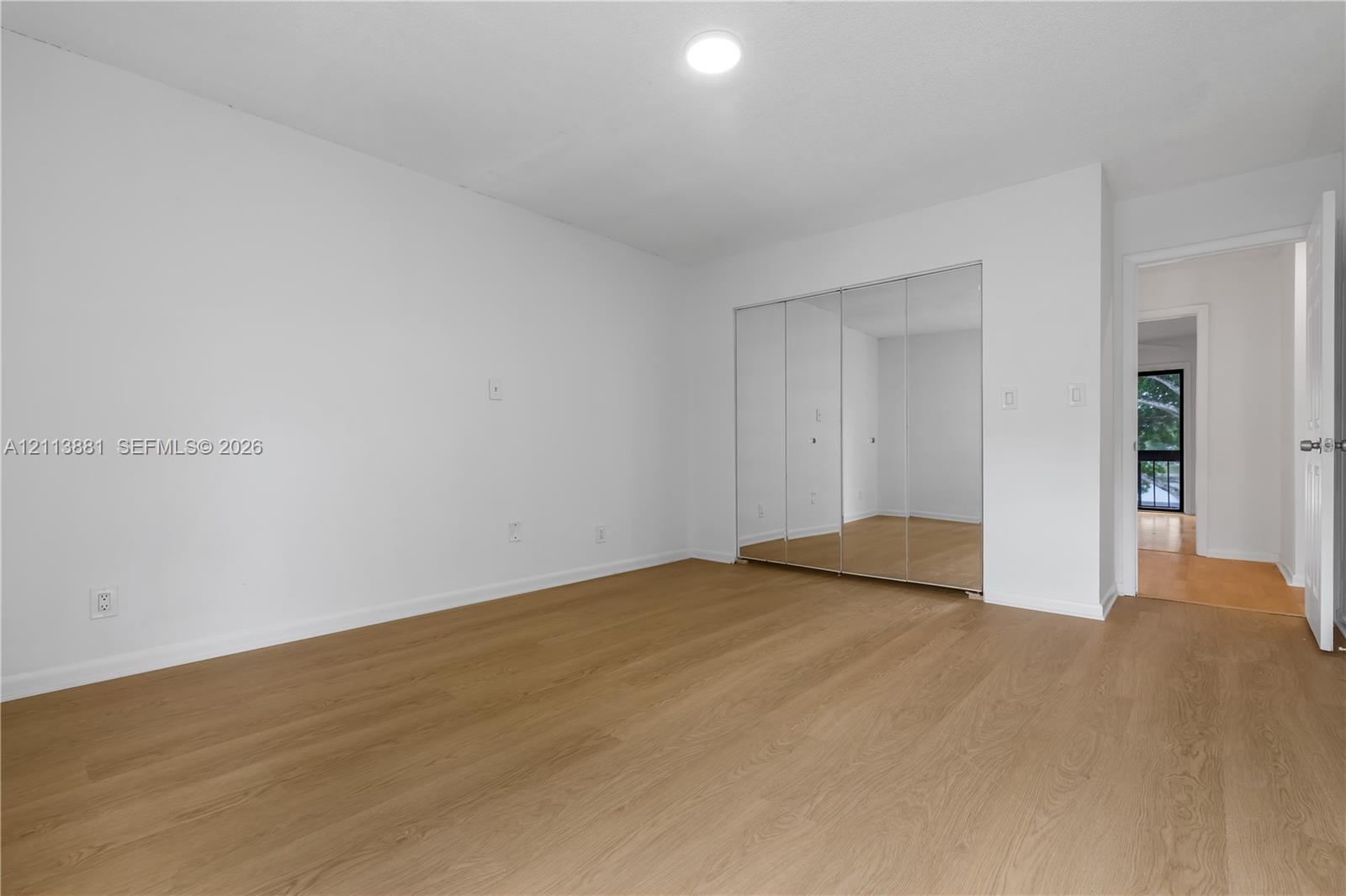 Neutral-toned interior featuring wood-finish flooring, white walls, and a built-in closet with mirrored sliding doors