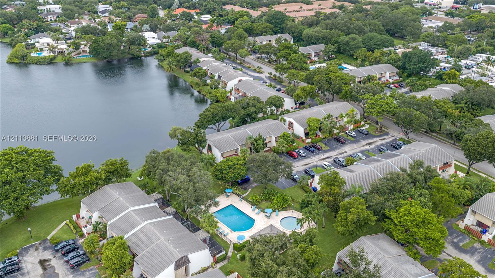 Aerial perspective featuring waterfront placement, community pool, spa, established landscaping, and paved parking