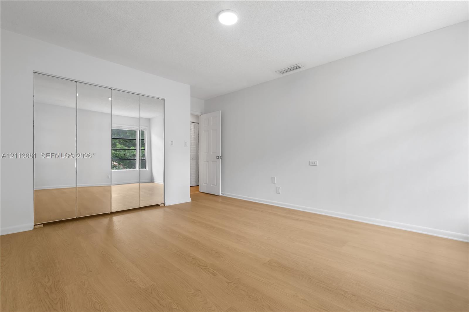 Room featuring wood-finish flooring, floor-to-ceiling mirrored sliding closet doors, a multi-panel door, and a single-light fixture