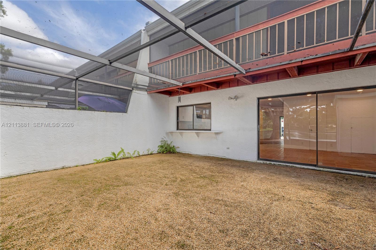 Screened outdoor area featuring a stucco wall, an upper-level balcony with a railing, and large sliding glass doors