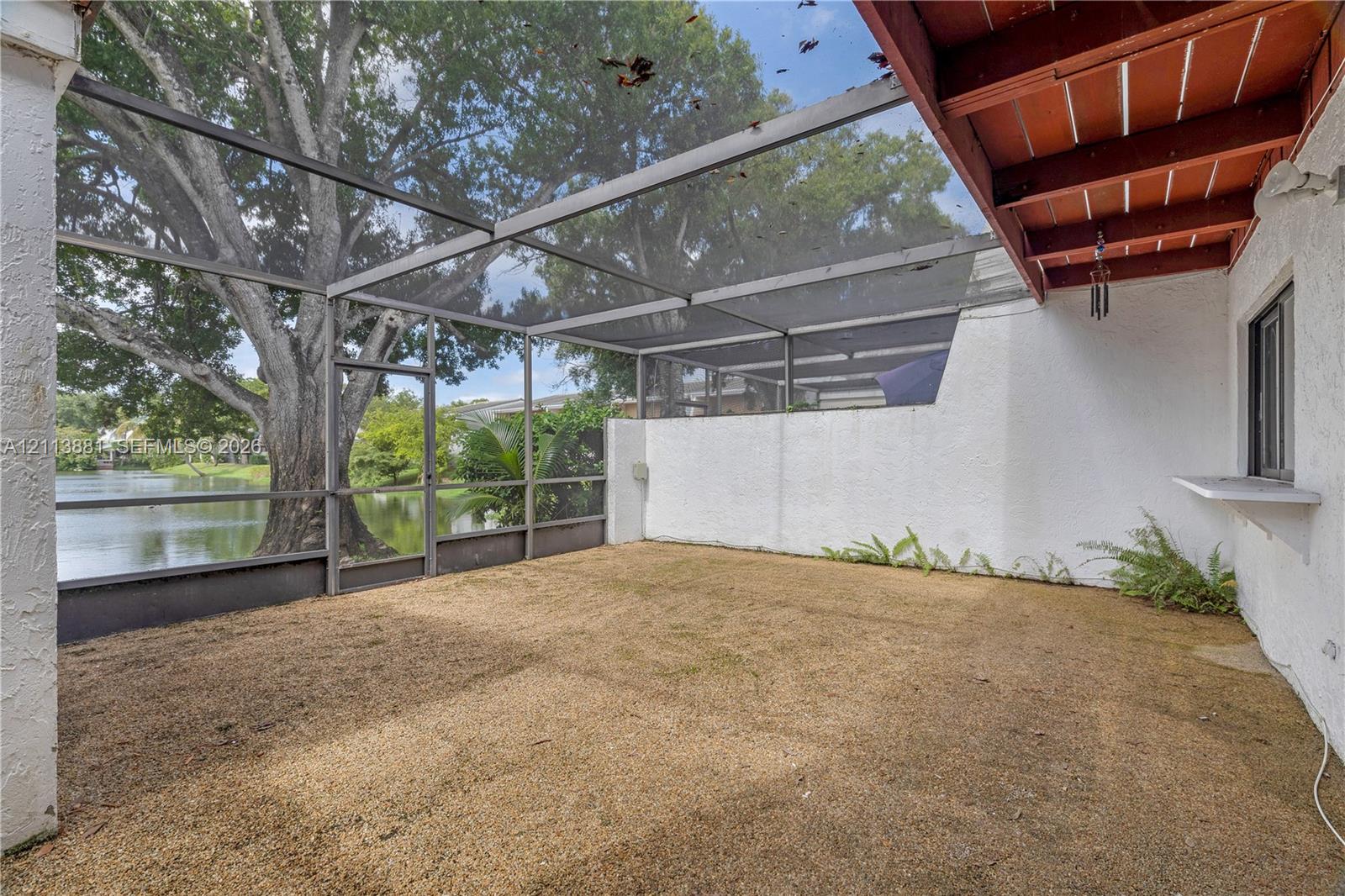 Screen-enclosed patio featuring exposed wood-beam ceiling, textured stucco wall, and exterior pass-through window overlooking water