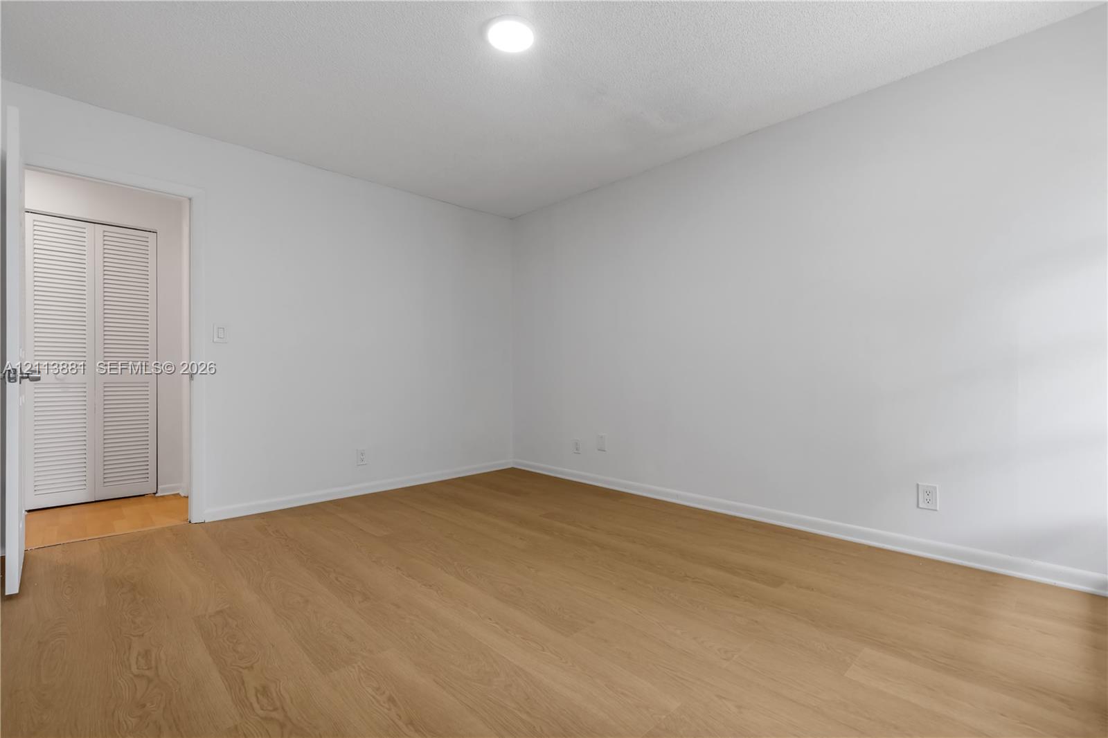 Wood-finish flooring, neutral walls, recessed ceiling lighting, and a closet with white louvered doors