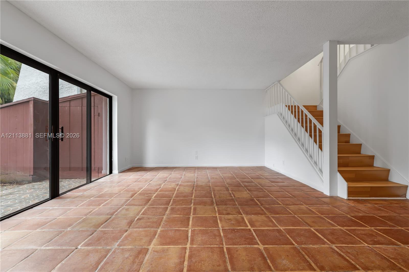 Living area featuring terracotta tile flooring, floor-to-ceiling sliding glass doors, and a staircase with wood-finish treads and white vertical railings