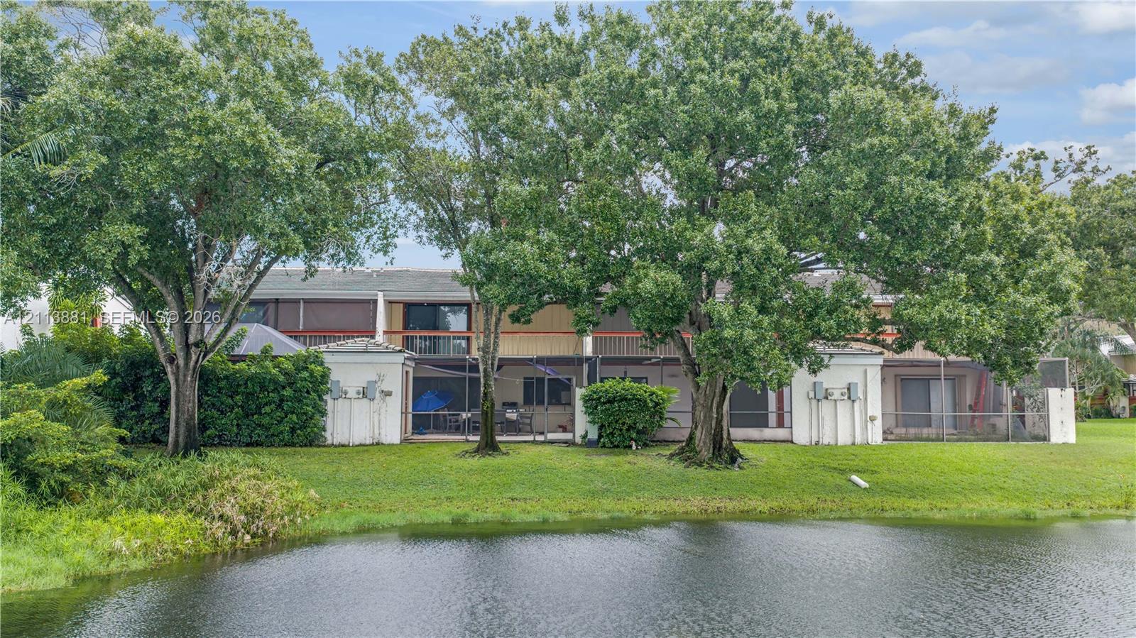 Exterior featuring waterfront positioning, multiple screened-in ground-level lanais, second-story balconies, and mature canopy trees