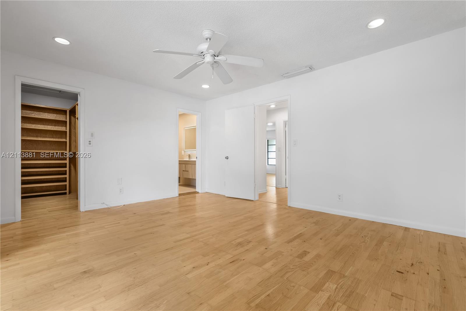 Interior room featuring wood-finish flooring, recessed lighting, white ceiling fan, and built-in closet shelving