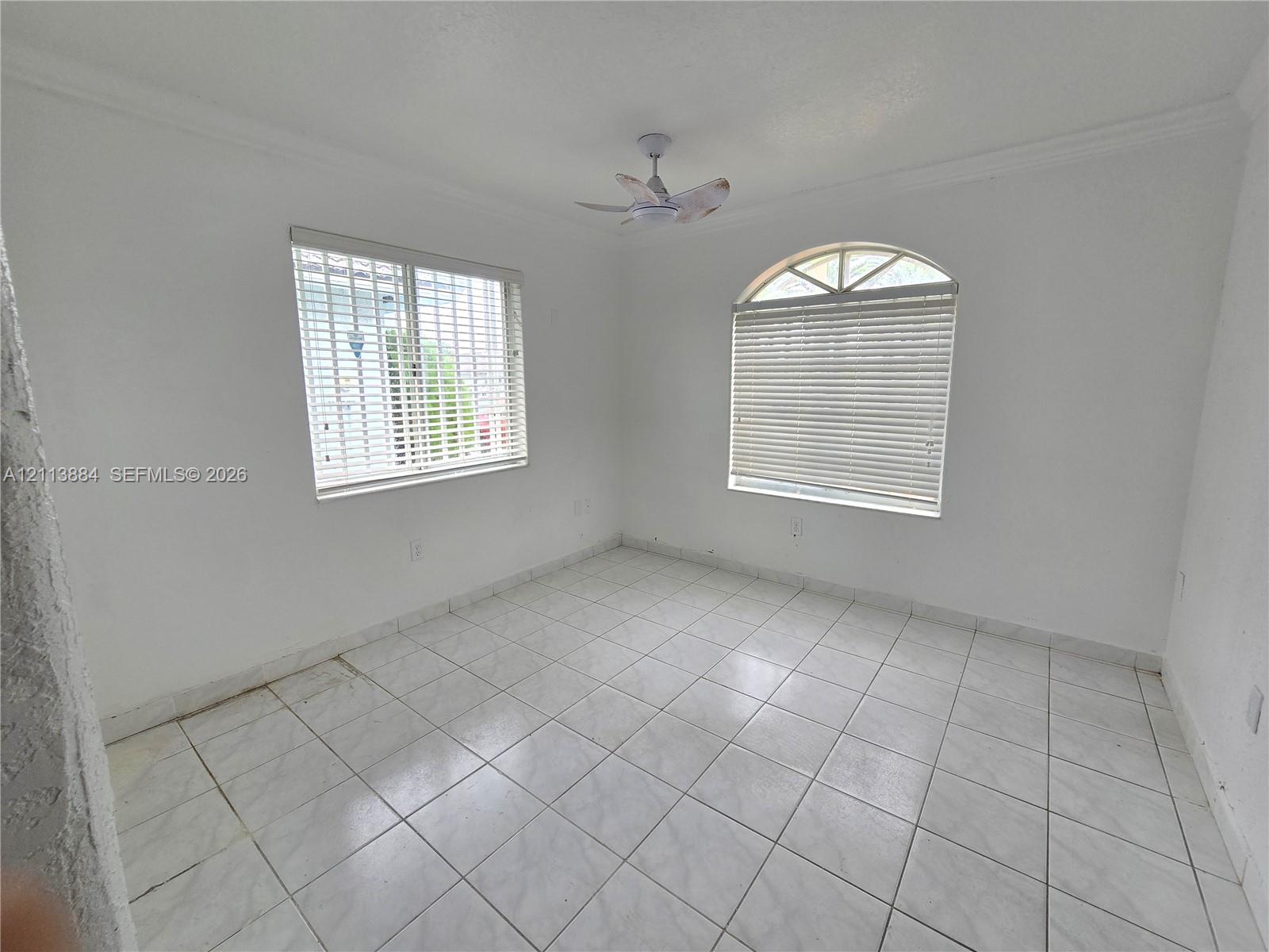 Room featuring white ceramic tile flooring, an arched window, a ceiling fan, and crisp crown molding