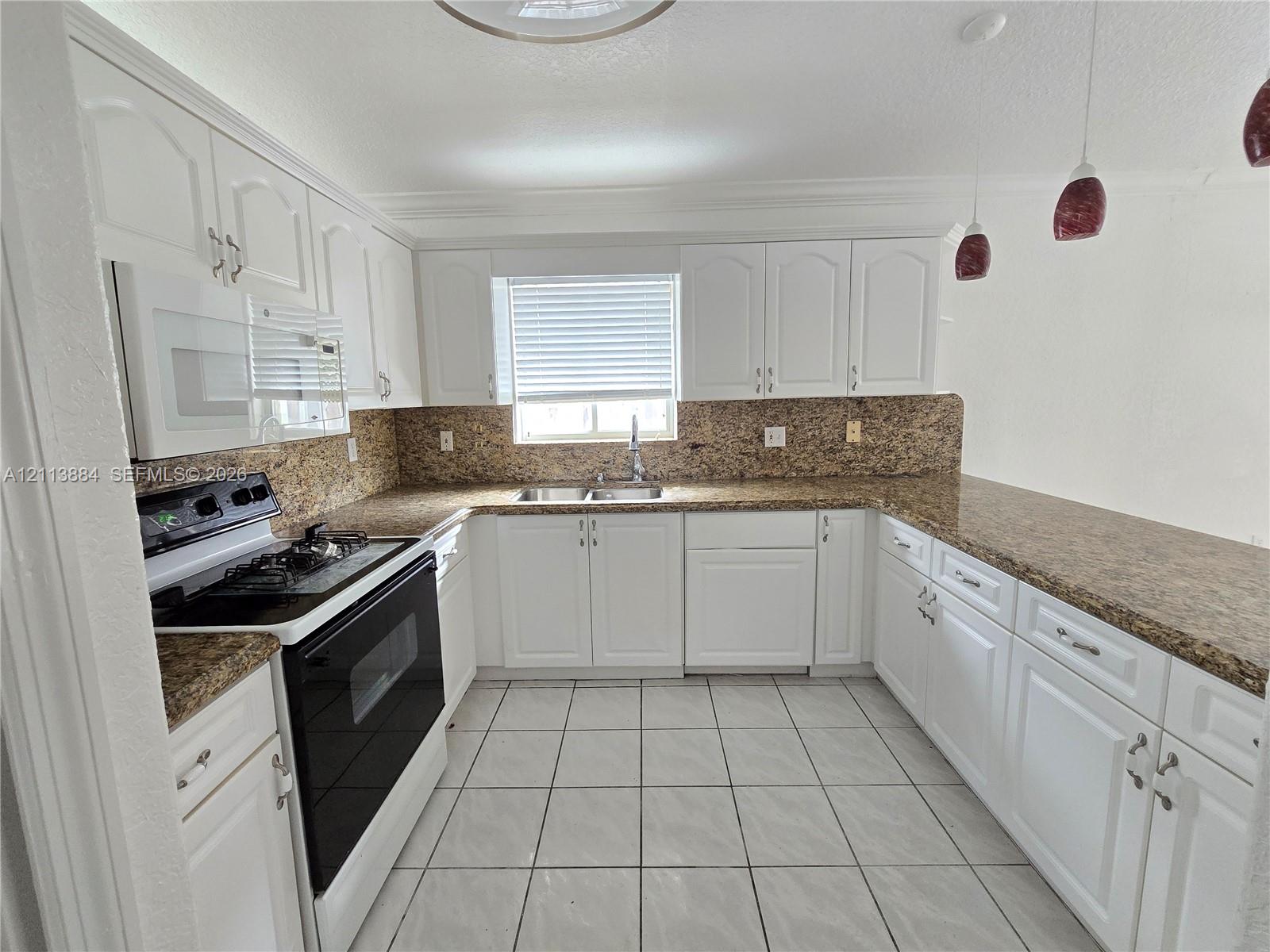 Kitchen featuring white cabinetry, stone-finish countertops, tile flooring, dual-basin sink, and integrated microwave