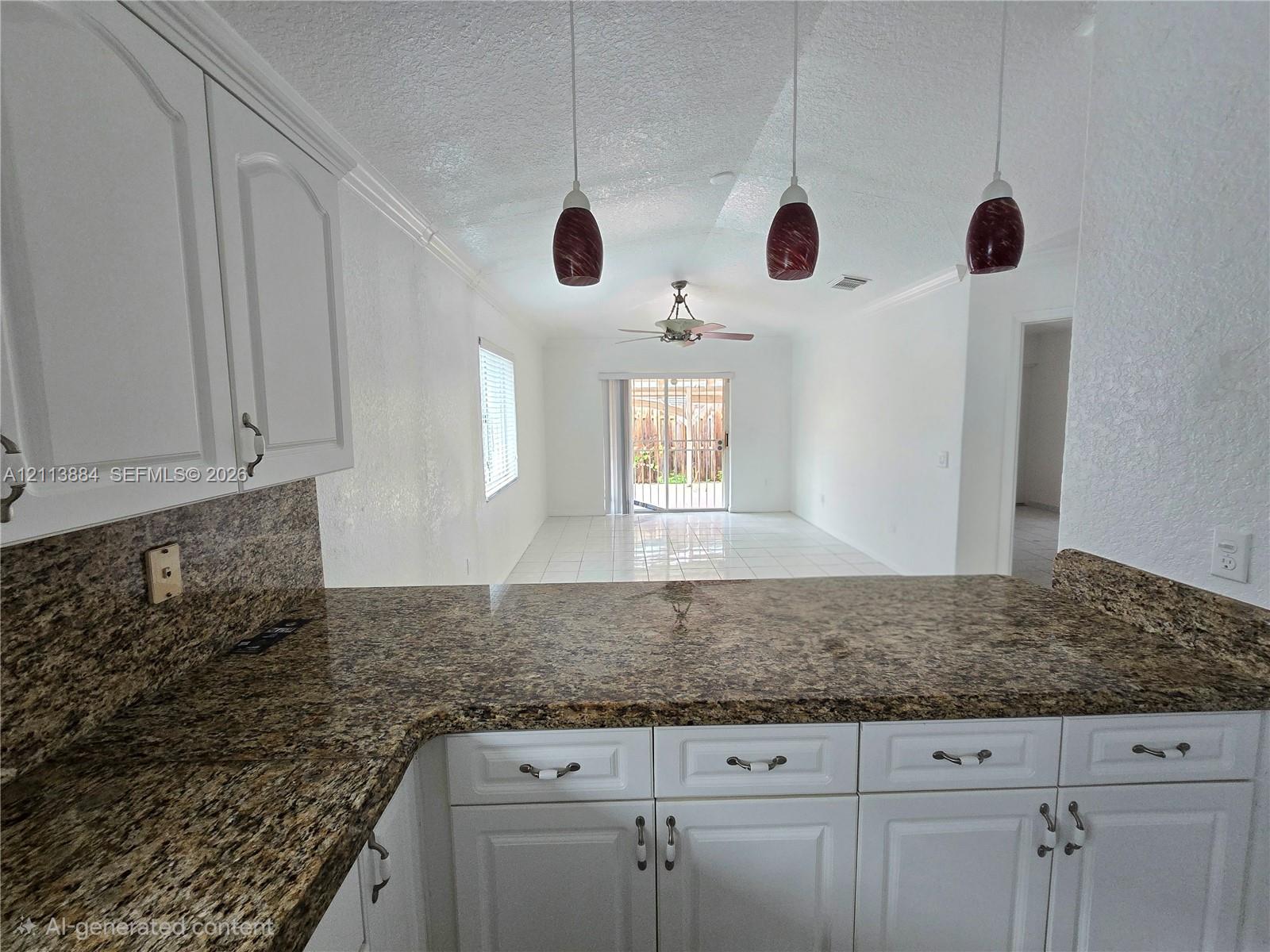 Kitchen featuring white shaker-style cabinetry, stone-finish countertops, three suspended pendant lights, and tile flooring