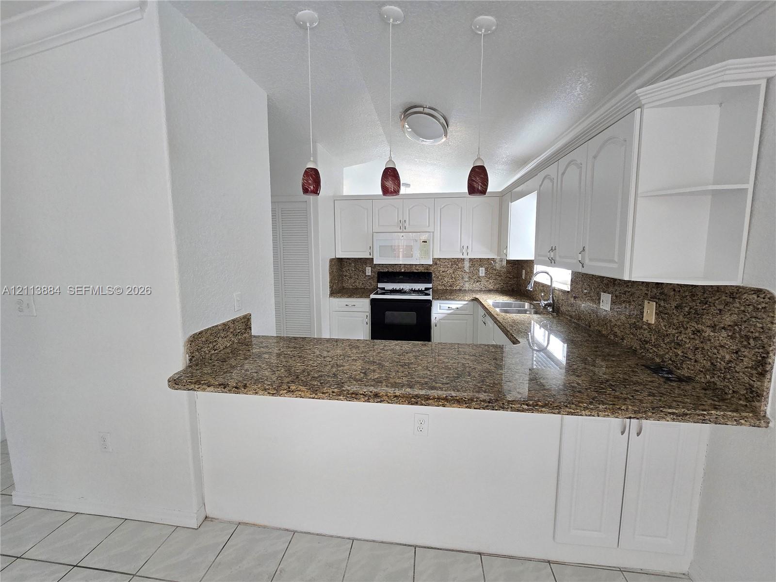 Kitchen featuring stone-finish countertops, white cabinetry, tile flooring, three pendant lights, and a built-in oven