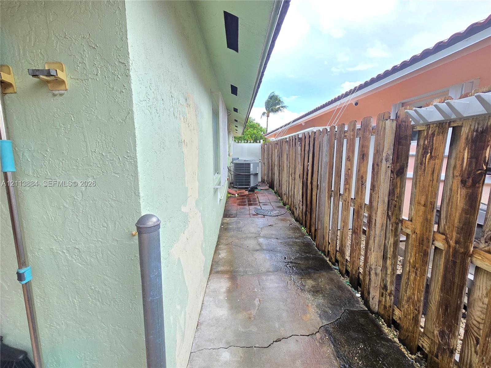 Side exterior area featuring a concrete pathway, vertical wood privacy fencing, and an external HVAC condenser unit