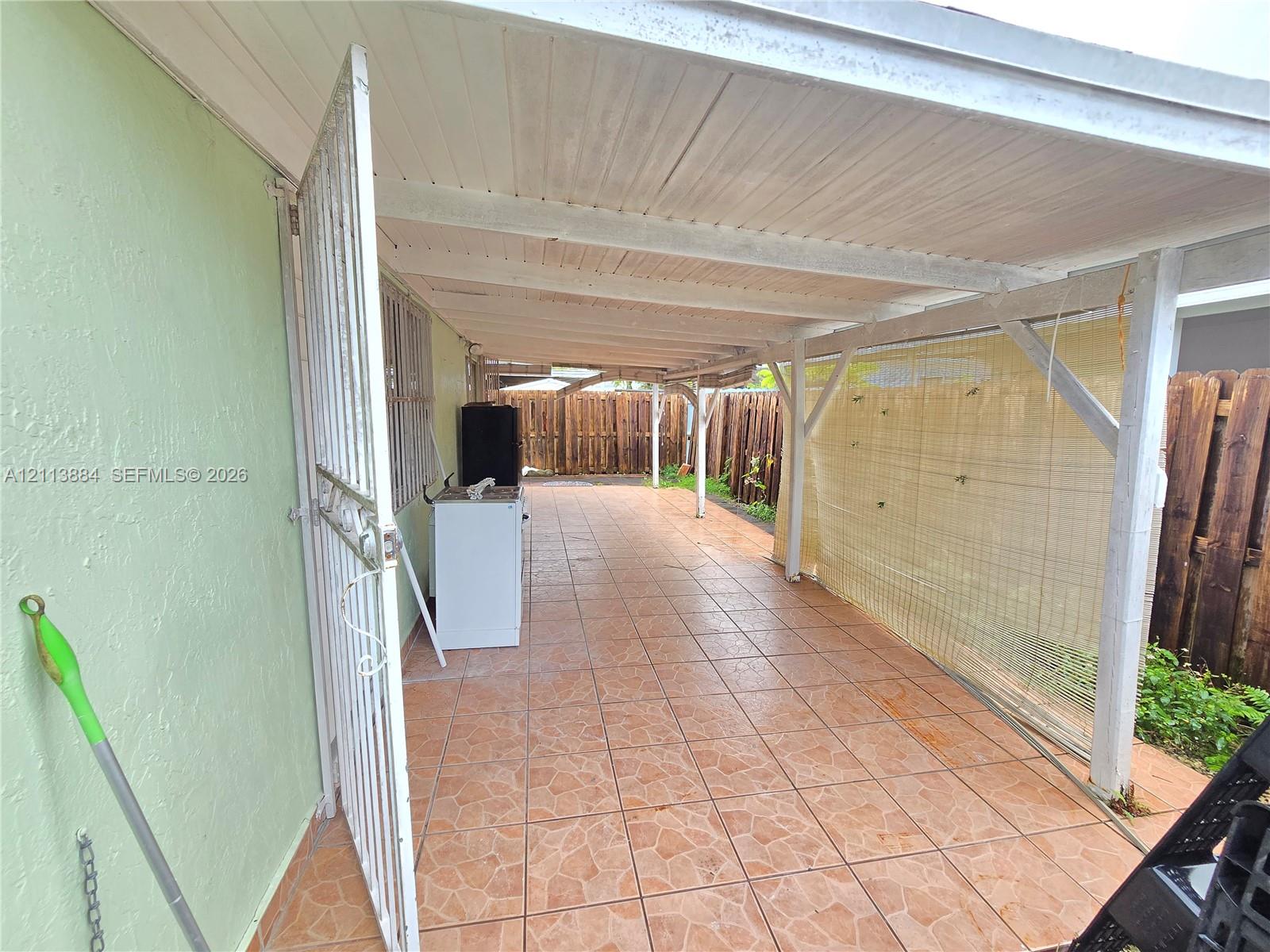 Covered patio featuring tiled flooring, a wooden support structure, and a perimeter wood-slat fence