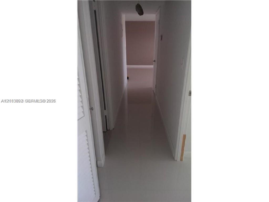 Hallway featuring neutral-toned tile flooring and louvered closet doors