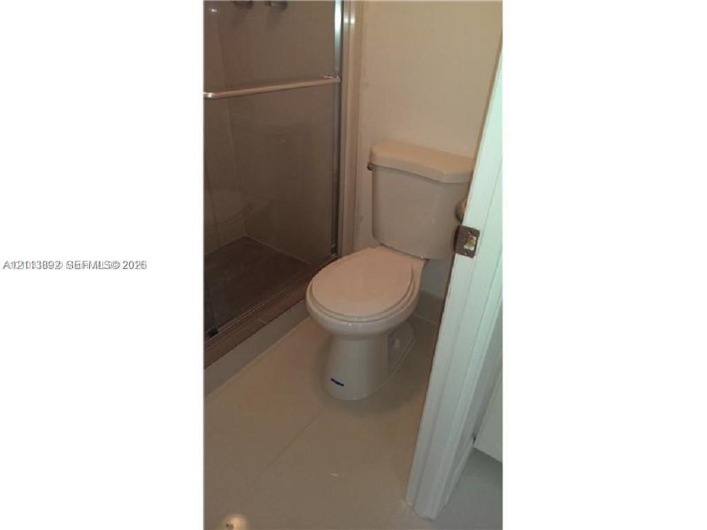 Enclosed shower with glass sliding doors and tile flooring, paired with a standard-profile toilet