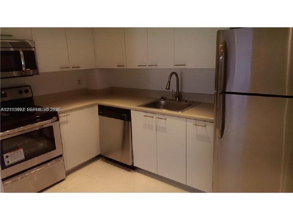 Kitchen featuring white cabinetry, stainless steel appliances, a pull-down faucet, and neutral countertops