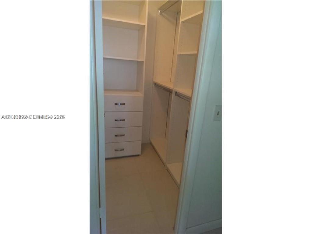 Walk-in closet featuring white built-in shelving, four integrated storage drawers with metal pulls, and hanging rods