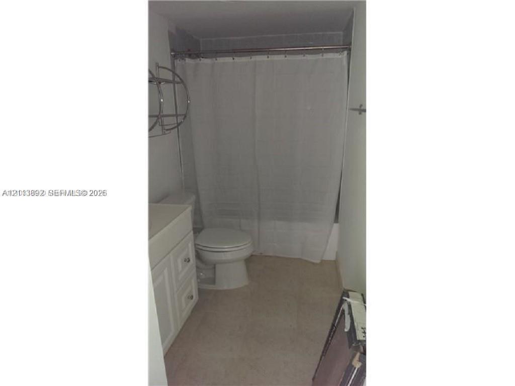 Bathroom featuring a white vanity cabinet with drawers, a toilet, and a tub-shower combination with a metal tension rod