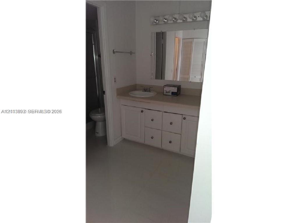 Bathroom vanity featuring solid-surface countertop with integrated oval sink, white cabinetry with hardware pulls, and wall-mounted light fixture above a rectangular mirror