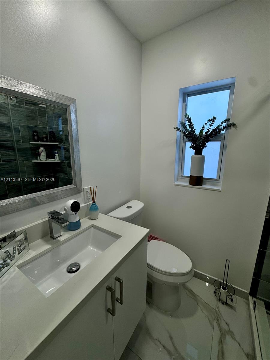 Bathroom featuring a vanity with a white rectangular sink and countertop, framed mirror, stone-finish floor tiling, and a vertical window