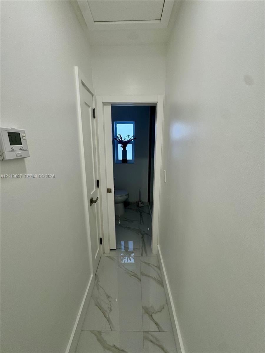 Hallway featuring large-format porcelain tile flooring with veining, a solid-core door with matte black hardware, and a programmable wall-mounted thermostat