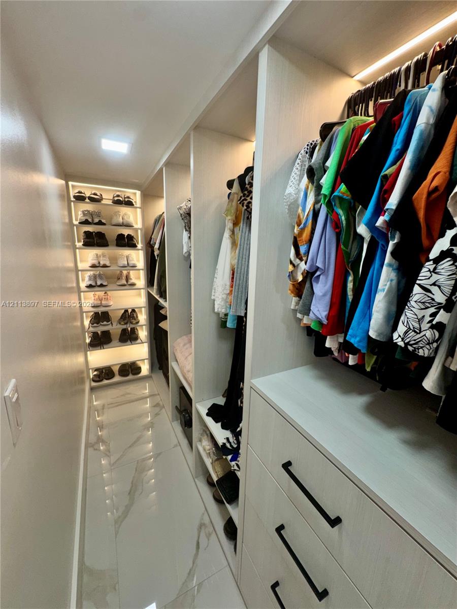 Custom walk-in closet featuring floor-to-ceiling built-in shelving, integrated LED accent lighting, three-drawer cabinetry with matte black hardware, and large-format porcelain tile flooring