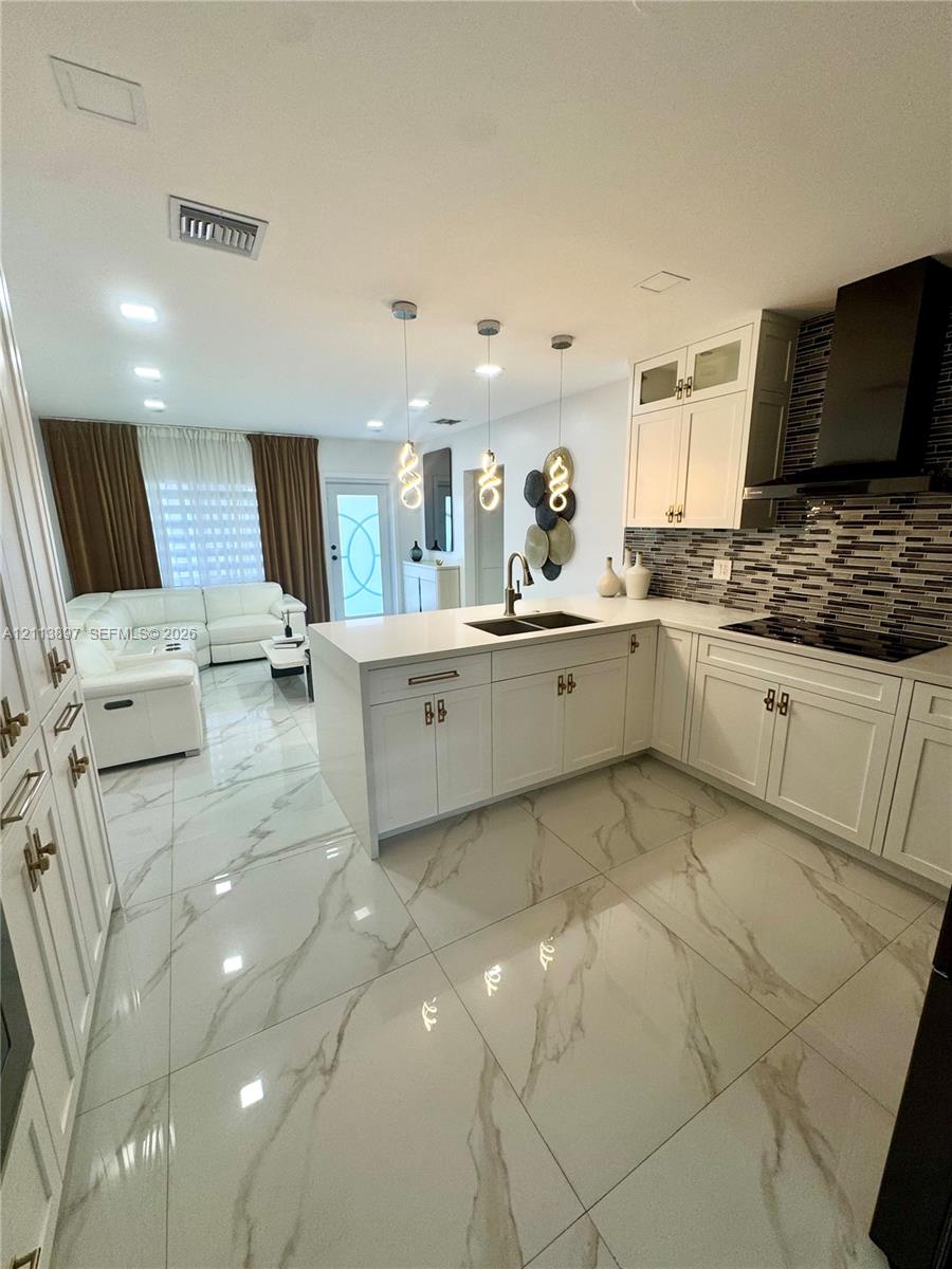 Kitchen featuring white cabinetry, solid-surface countertops, a tiled backsplash, large-format veined flooring, and three pendant light fixtures