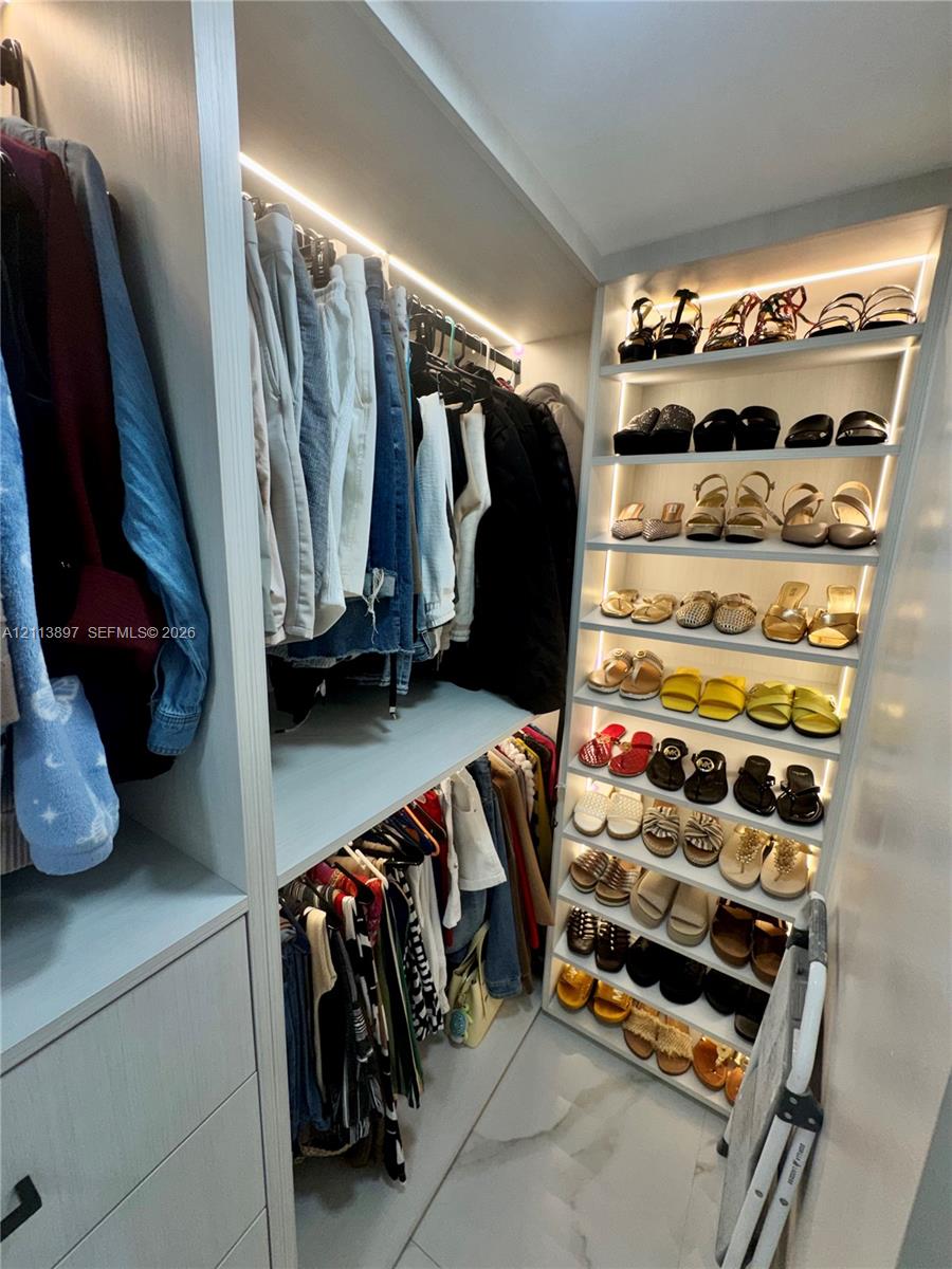 Custom walk-in closet featuring floor-to-ceiling shelving, integrated LED accent lighting, multi-level hanging rods, and large-format tile flooring