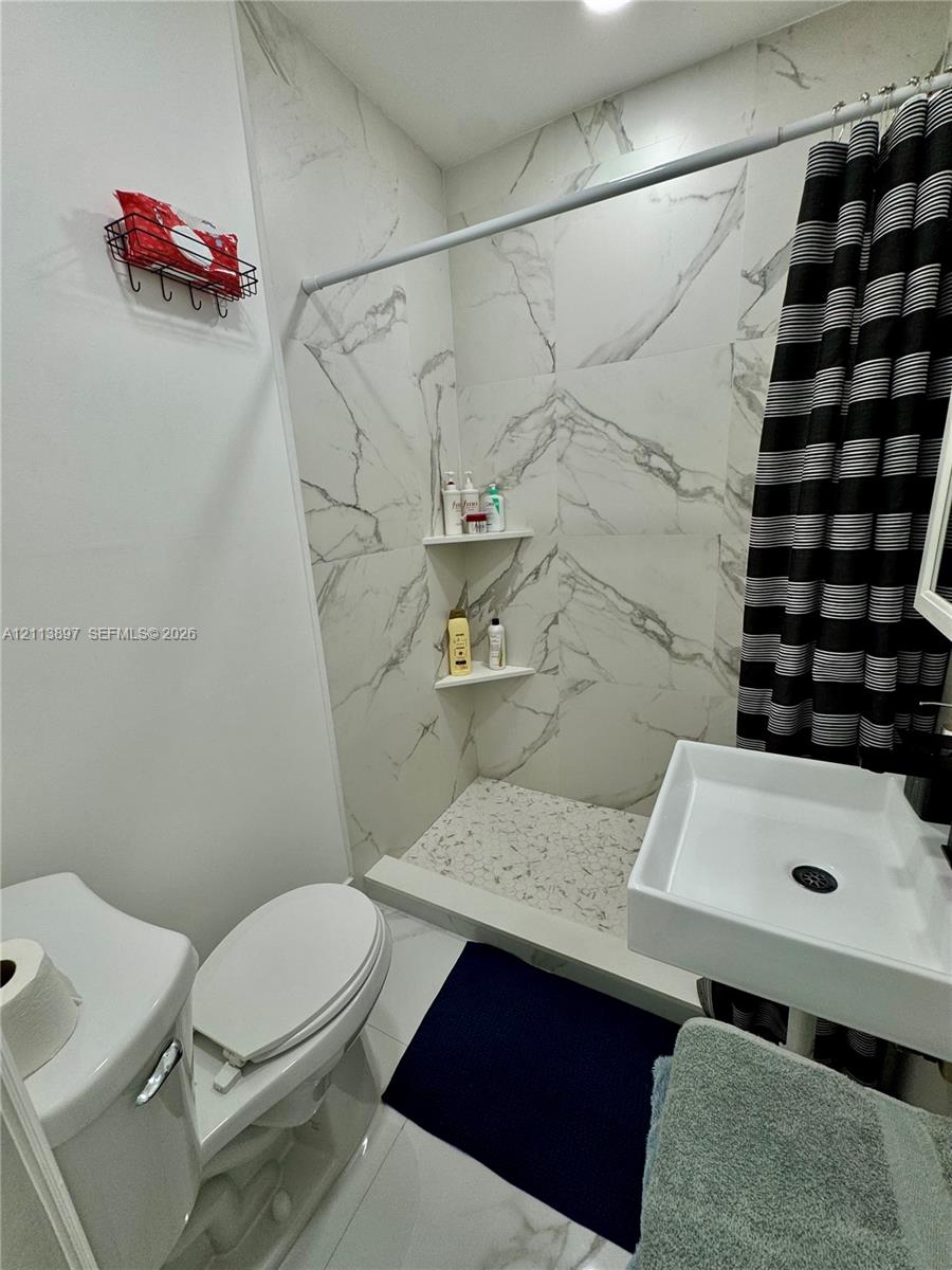 Full-height shower surround with white stone-patterned tile, integrated corner shelving, built-in pebble-finish shower floor, and a wall-mounted rectangular basin