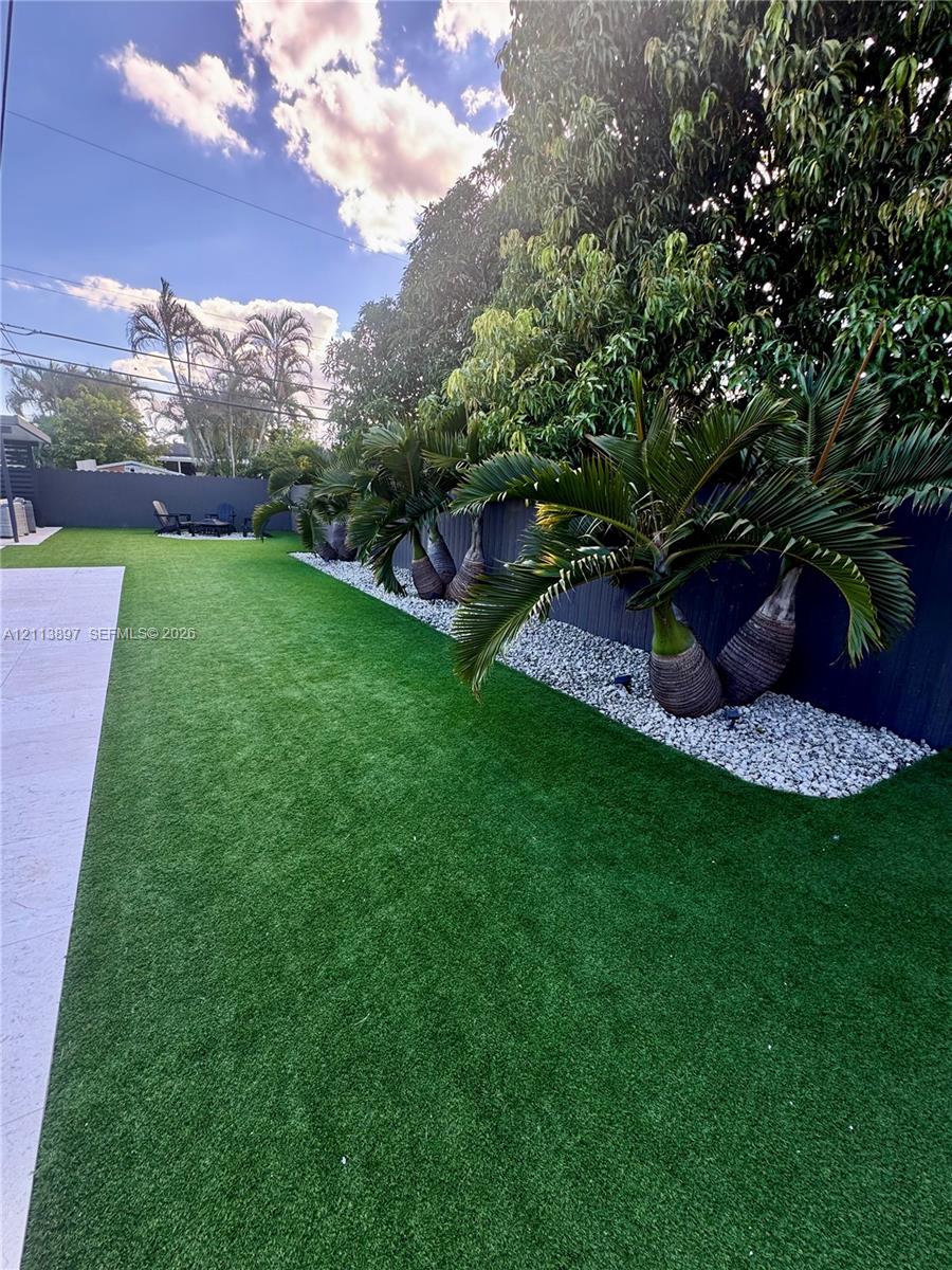 Manicured synthetic lawn, perimeter privacy fencing, and stone-accented landscaping with mature palm trees