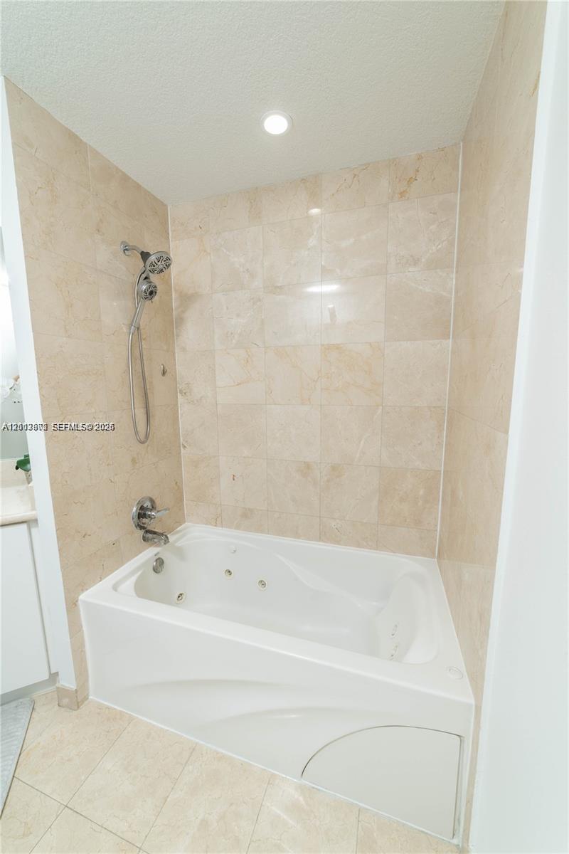 Built-in jetted soaking tub featuring full-height light-toned tile surround, integrated handheld shower fixture, and polished chrome faucet