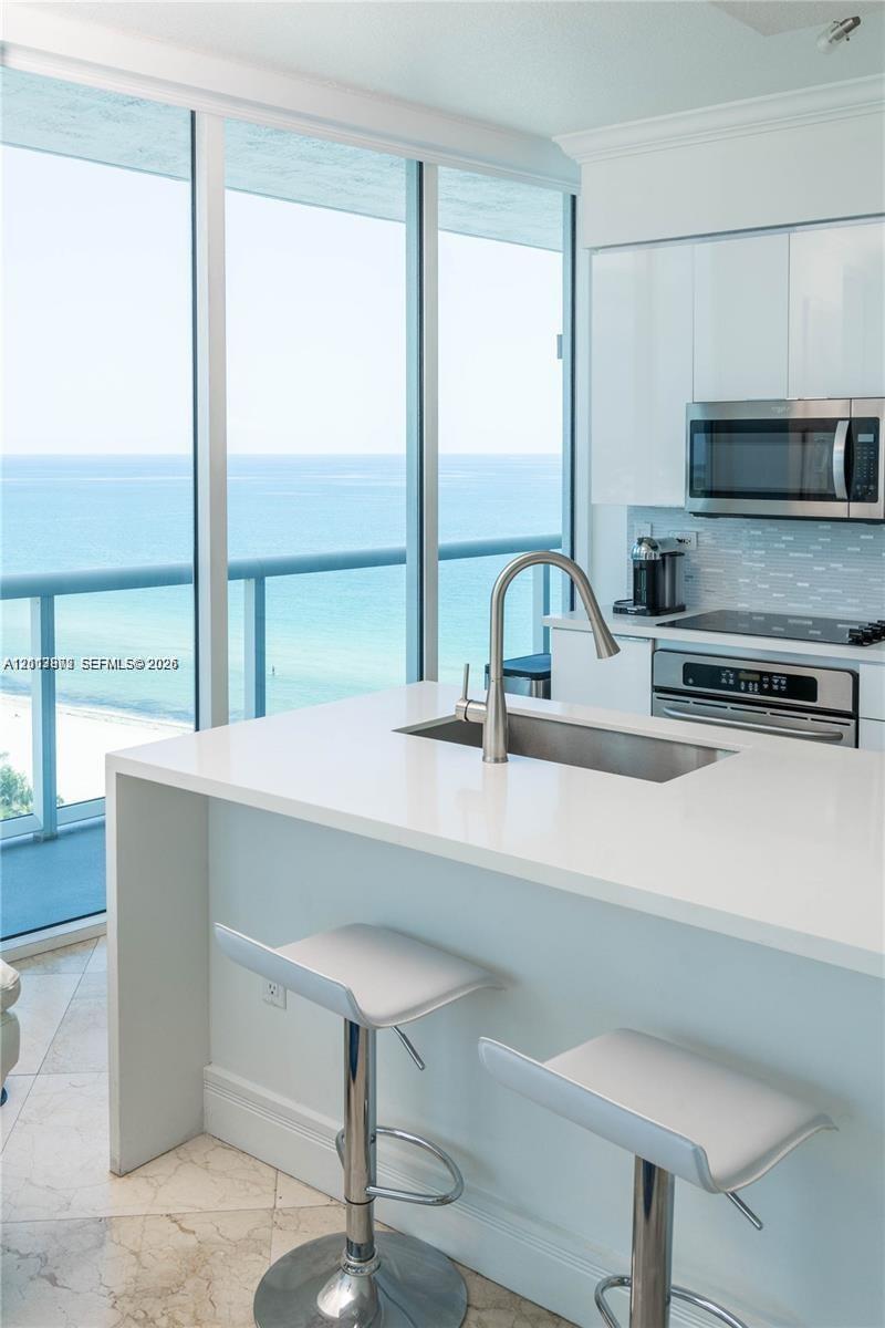 Kitchen featuring an eat-in waterfall island, quartz countertops, stainless steel undermount sink, floor-to-ceiling windows, and ocean backdrop