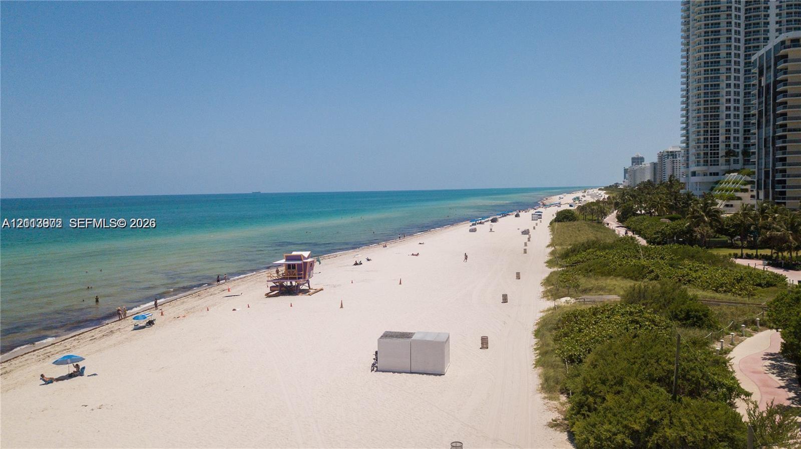 Direct oceanfront access featuring expansive sandy shoreline, turquoise water, and tropical foliage