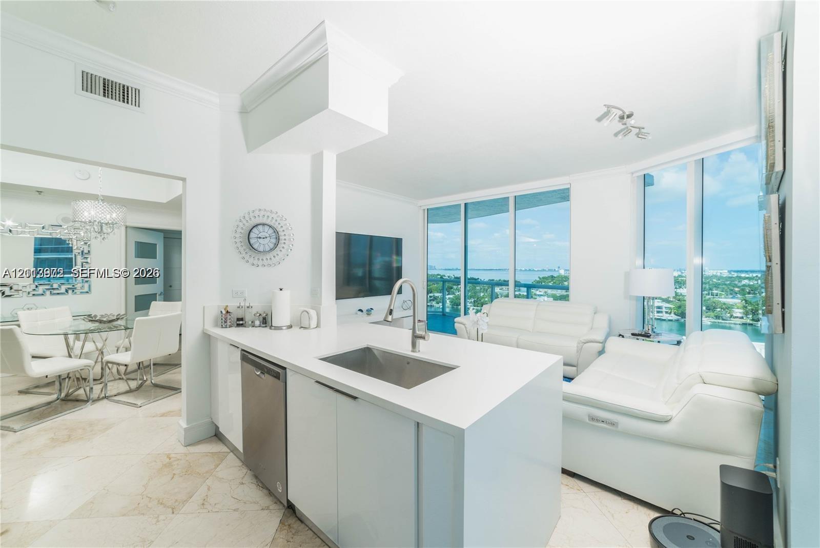 Kitchen island with stone countertop, stainless steel under-mount sink, integrated stainless steel dishwasher, and floor-to-ceiling windows