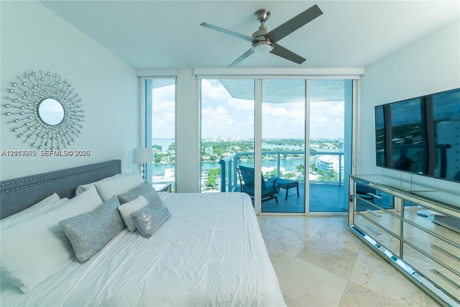 Floor-to-ceiling glass sliding doors, polished stone flooring, balcony access, and a ceiling-mounted fan