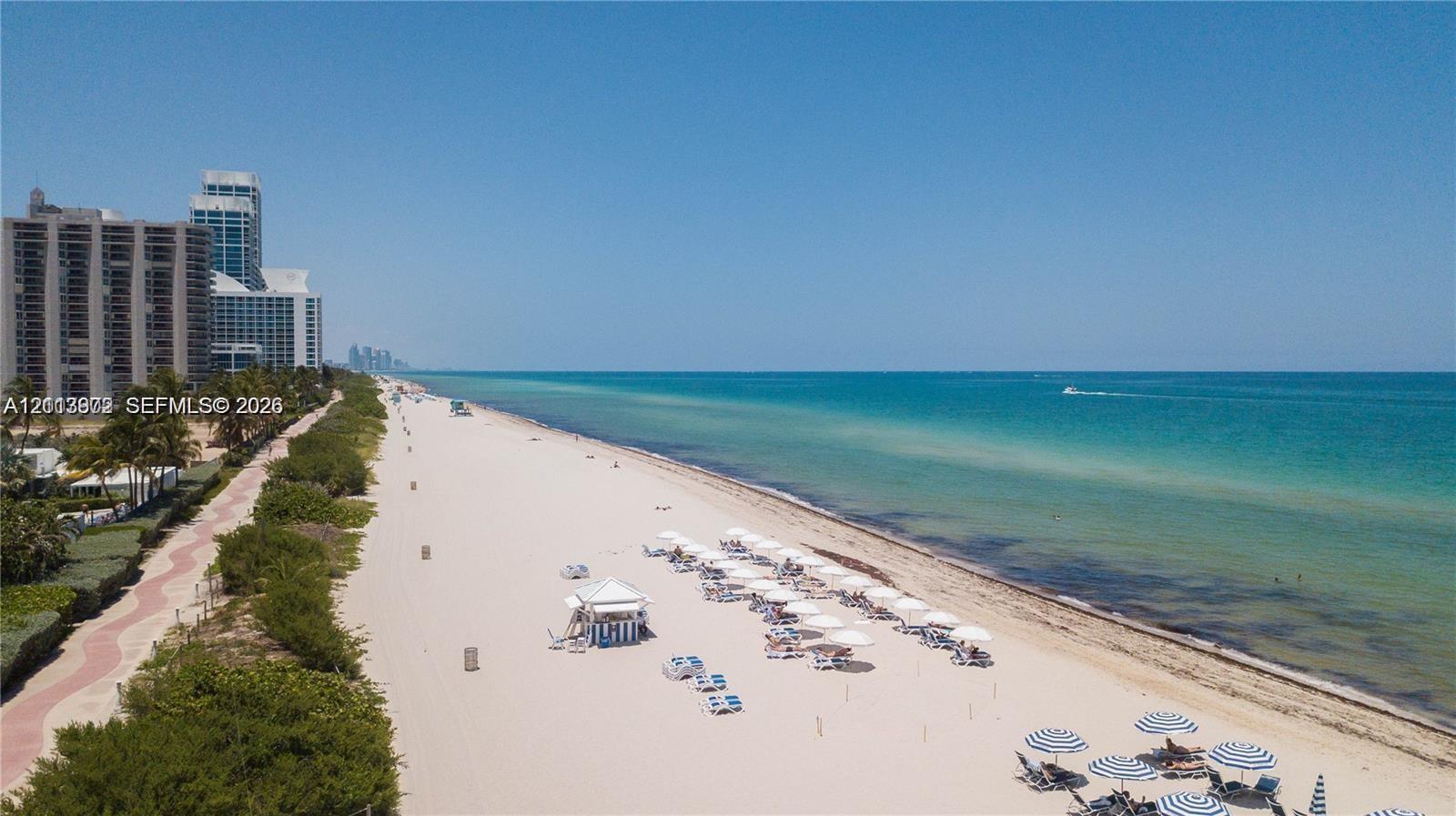 Coastal stretch featuring expansive sand beach, paved shoreline pathway, and direct oceanfront access
