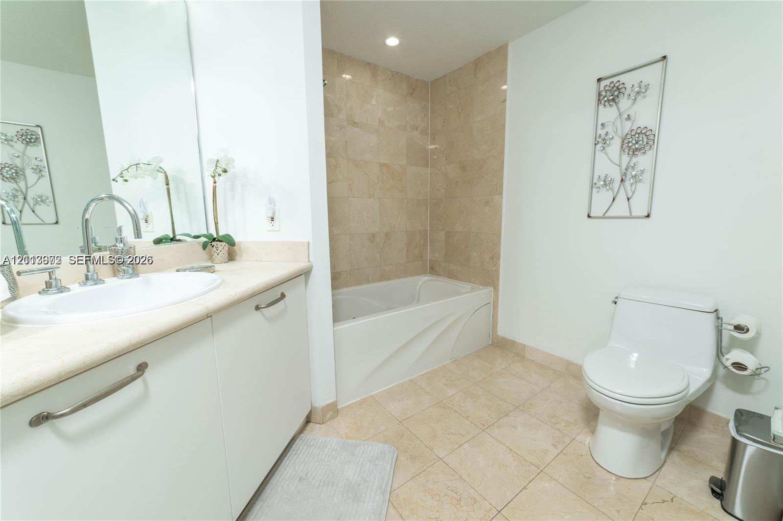 Bathroom featuring a vanity with an integrated basin, neutral stone-finish wall tile surrounding the bathtub, and light-toned floor tiling