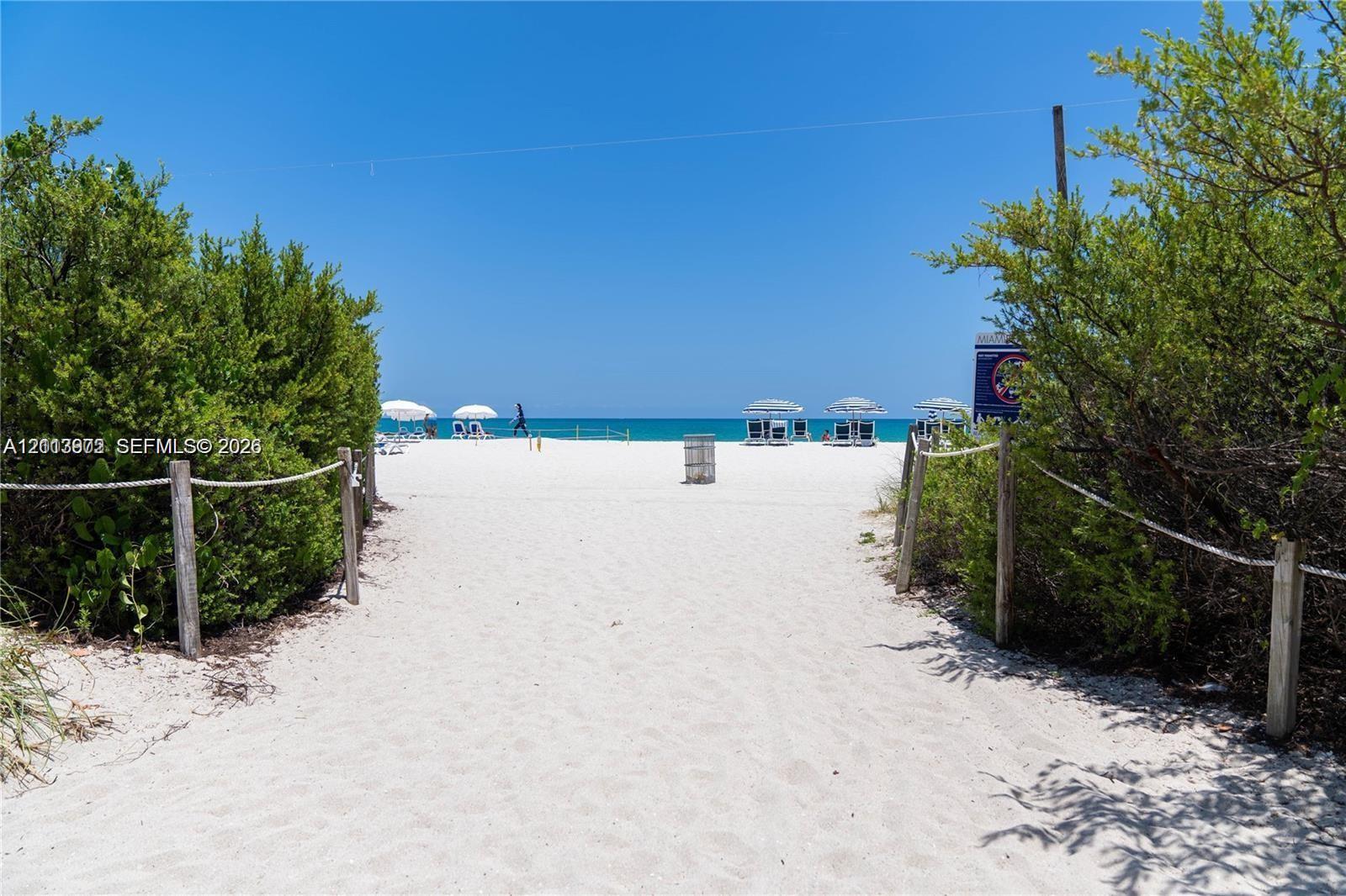 Sandy beach access path featuring natural vegetation, wooden post-and-rope fencing, and direct oceanfront location
