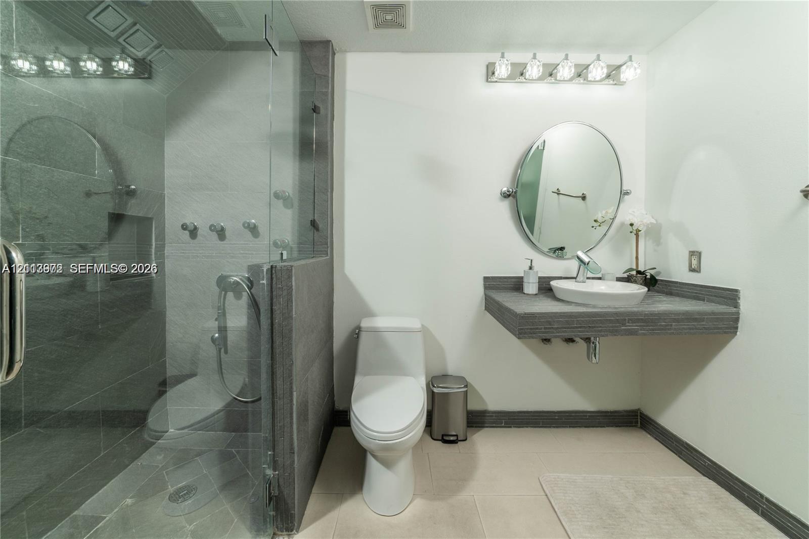 Floating vanity with a vessel sink, glass-enclosed shower with tiled walls, and polished light fixtures
