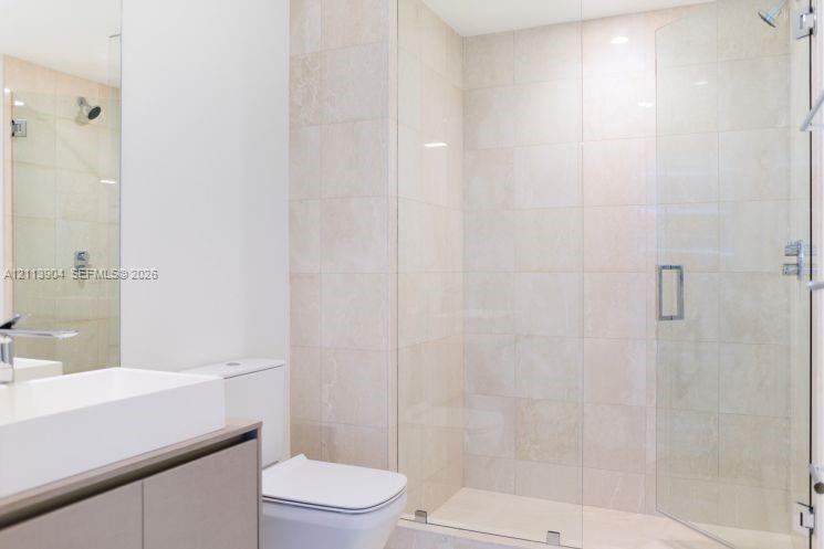 Walk-in shower with floor-to-ceiling neutral tile, frameless glass enclosure, wall-mounted shower head, and built-in vanity with a rectangular basin