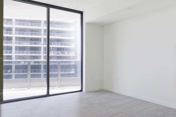 Floor-to-ceiling glass sliding door, neutral wall finishes, wood-finish flooring, and an attached balcony